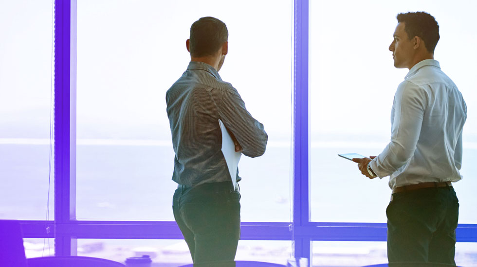 two men in discussion in front of a large window